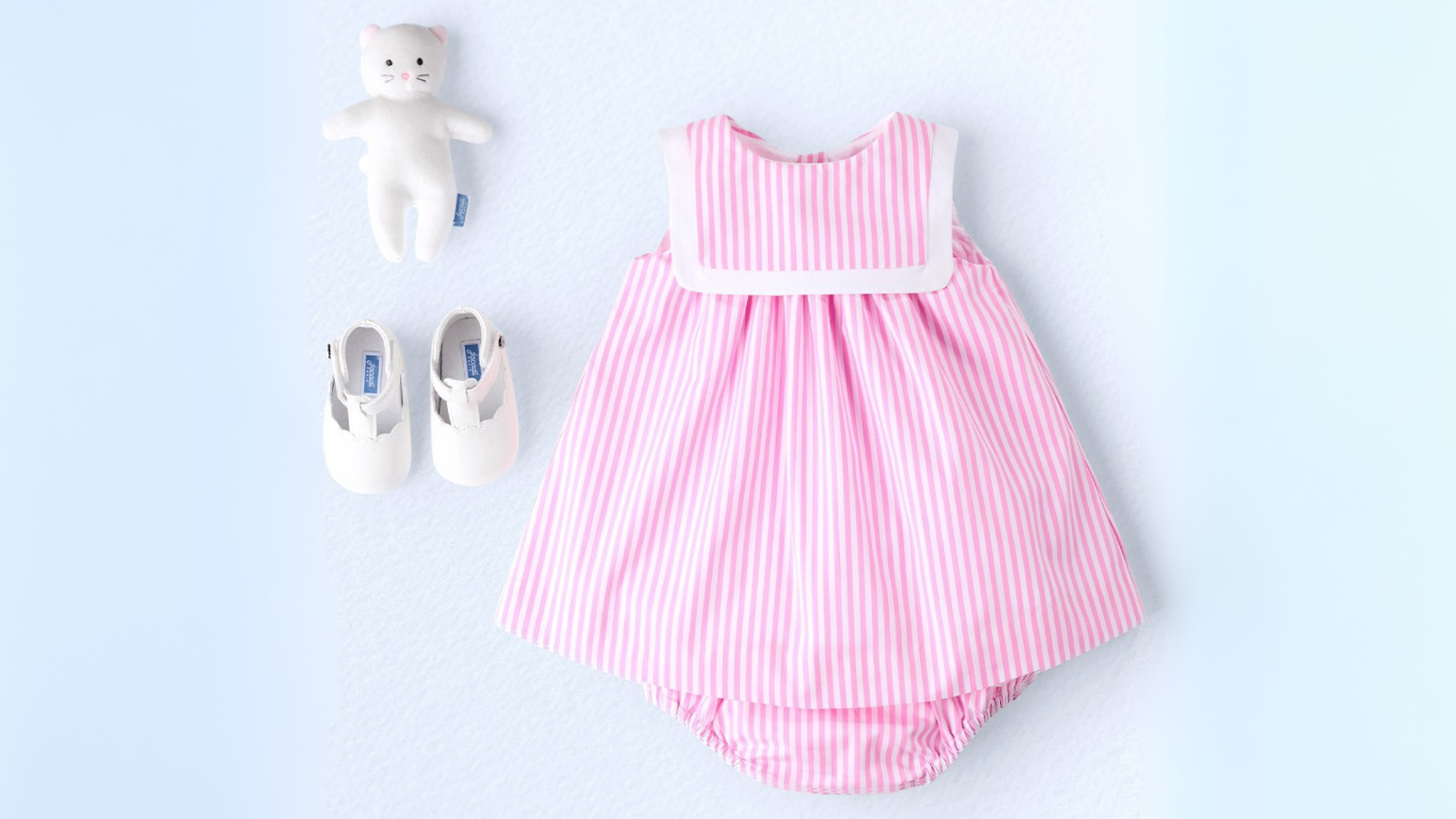 Carefully folded luxury baby clothes and travel essentials laid out for packing, featuring soft onesies